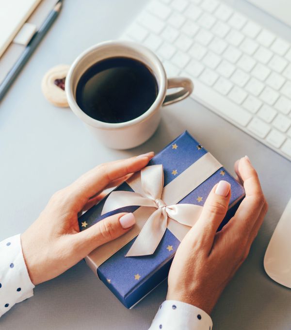 Hands wrapping blue gift with coffee on desk